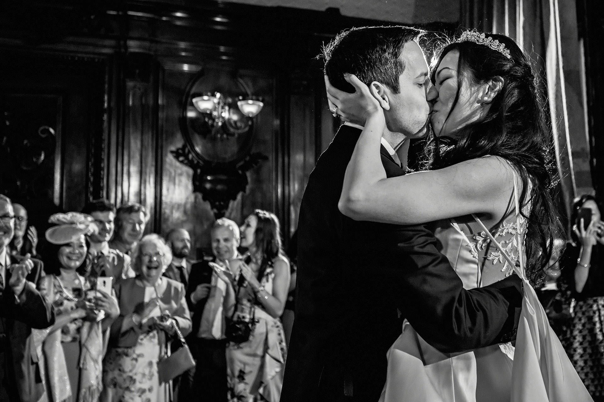 bride and groom kiss during first dance with family looking on 